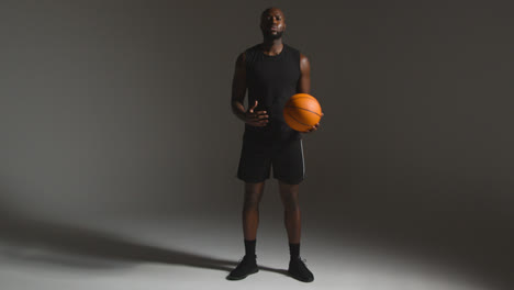 Studioporträt-In-Voller-Länge-Eines-Männlichen-Basketballspielers,-Der-Vor-Dunklem-Hintergrund-Den-Ball-Von-Hand-Zu-Hand-Wirft